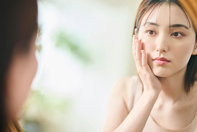 左手を頬に当てて鏡を見る女性